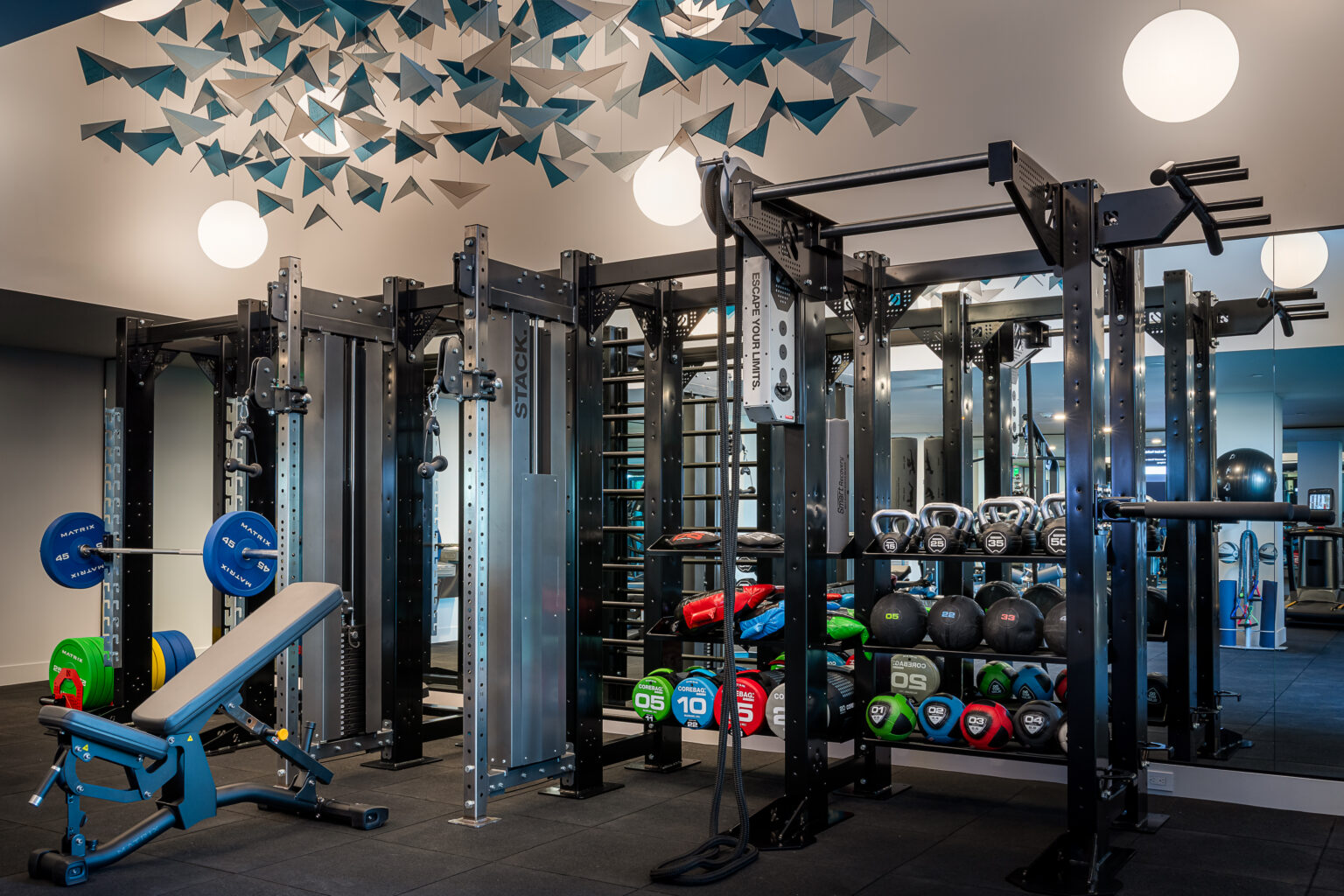 Gardena, CA, Apartments Near L'Oreal - Apollo South Bay - Fitness Center With Strength Training Racks, Free Weights, Kettlebells, Weight Bench, Mirrors, and Modern Overhead Lighting.